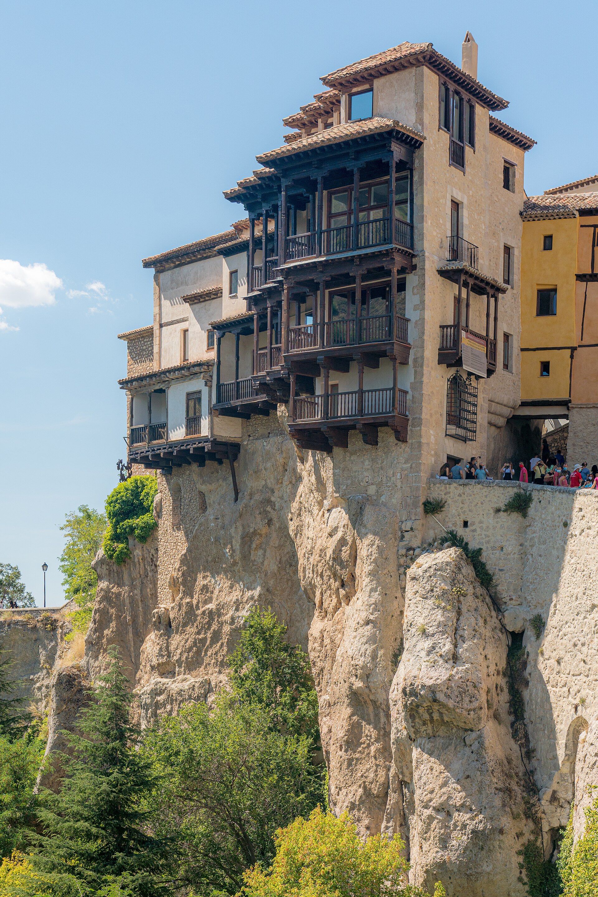 Casas Colgadas de Cuenca: balcones de madera sobre el tajo, turistas en el muro y vegetación abajo.