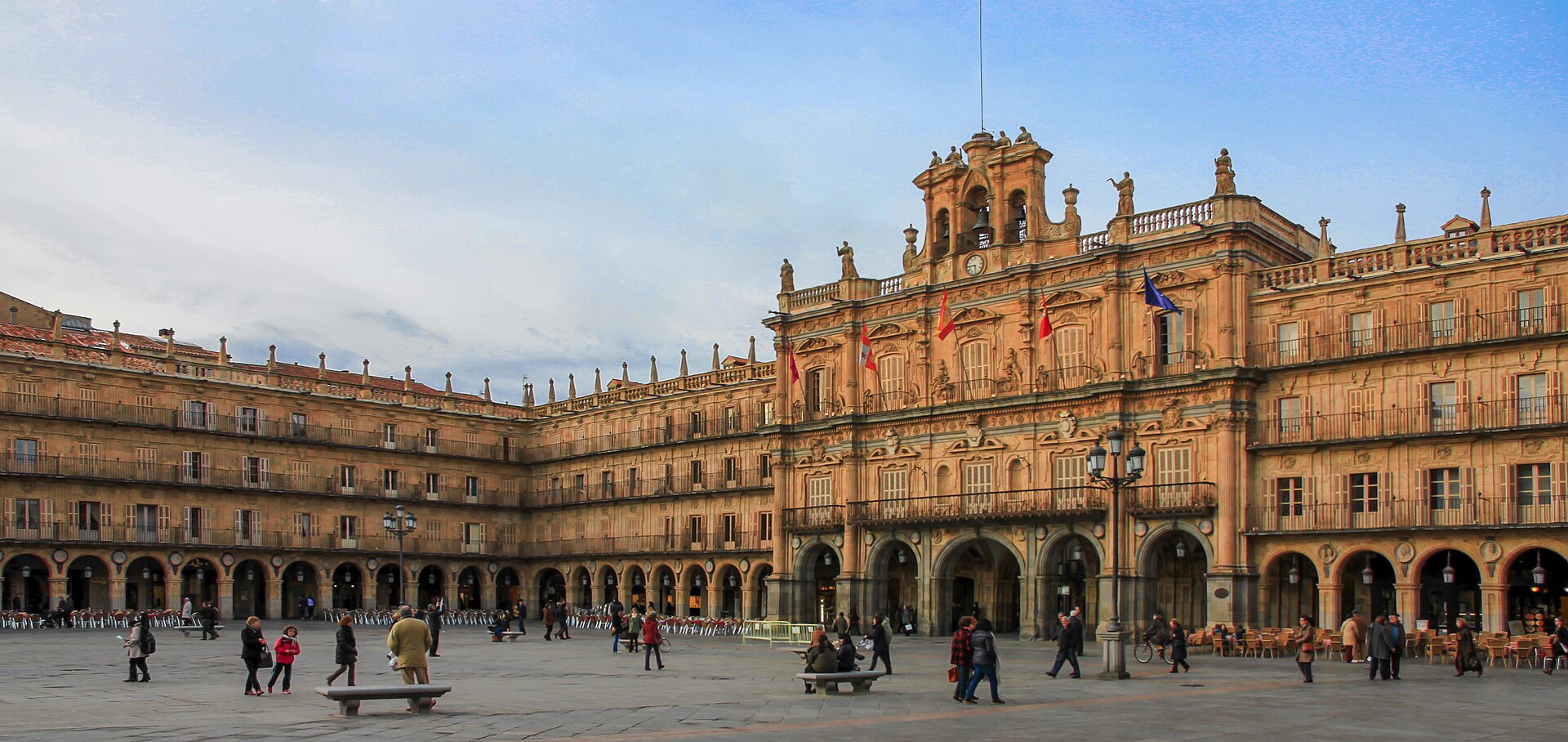 Plaza Mayor de Salamanca: pabellón del Ayuntamiento con reloj y banderas, soportales y gente en el empedrado.